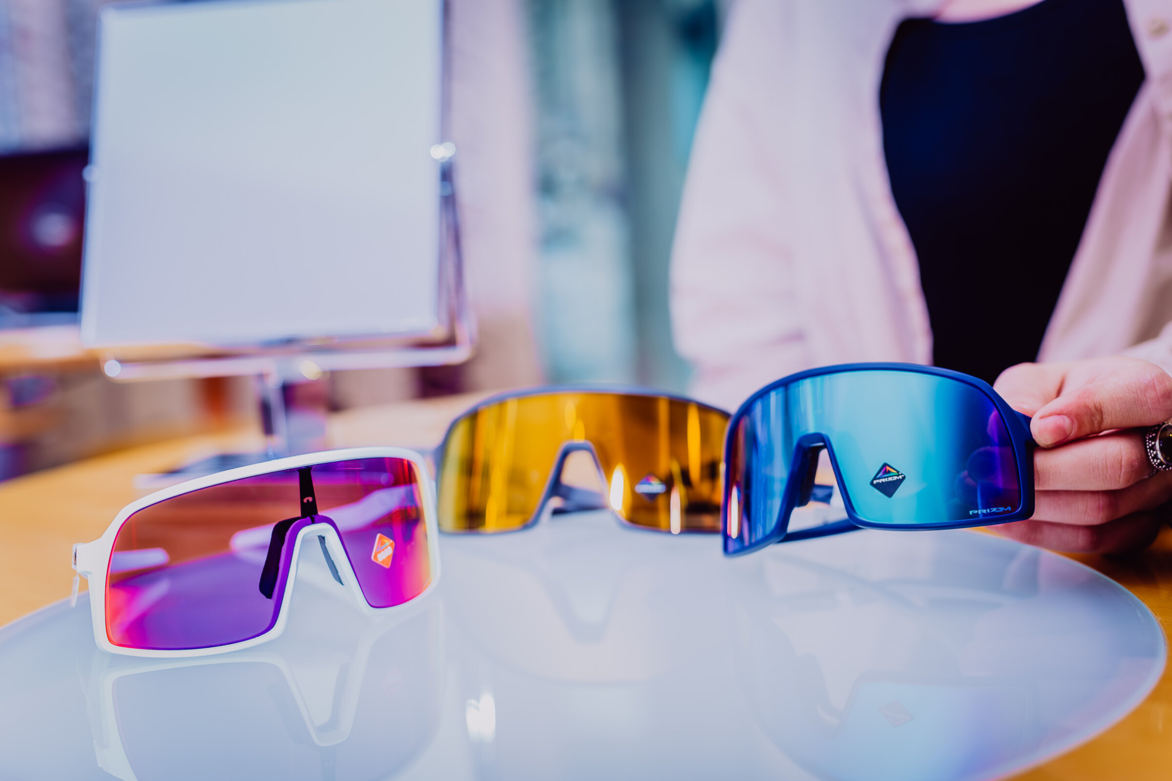Sportbrillen in verschiedenen Ausführungen auf einem Tisch. Blaue Sportbrille wird angehoben.
