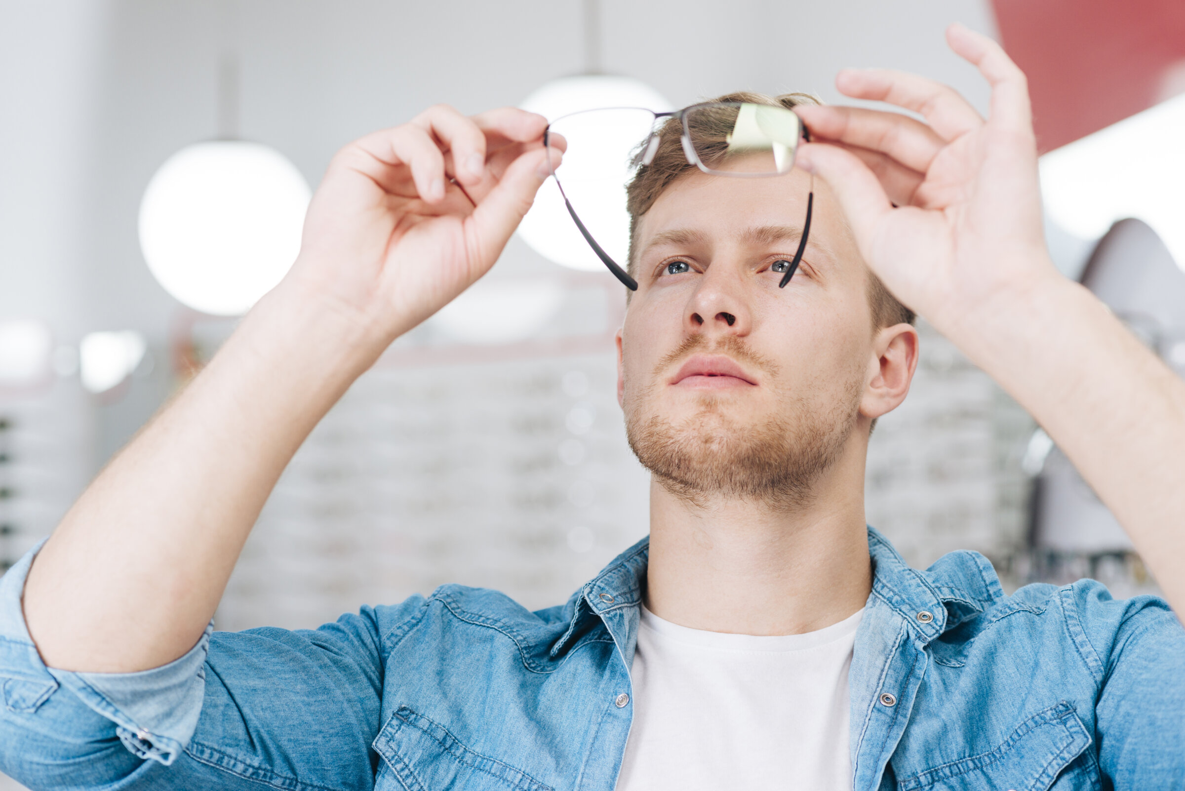Brille prüfen und anpassen lassen – was tun, wenn sie nicht richtig sitzt? Junger Mann prüft eine Brille im Optikergeschäft vor dem Aufsetzen – Beitragsbild für den Ratgeber zu rutschenden oder drückenden Brillen.