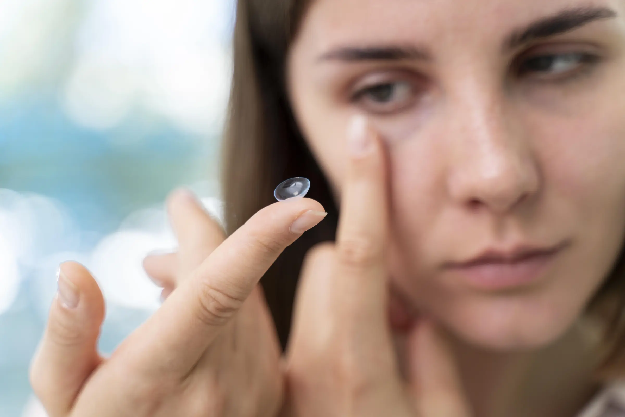 Junge Frau hält eine Kontaktlinse auf dem Finger und bereitet sich darauf vor, sie ins Auge einzusetzen – Symbolbild für das Einsetzen von Kontaktlinsen.