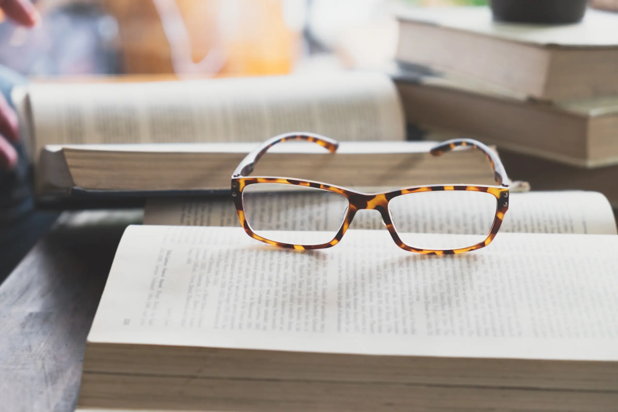 Beitragsbild2_Lesebrille Lesebrille mit braunem Muster liegt auf einem geöffneten Buch – Symbolbild für konzentriertes Lesen, Lernphasen oder altersbedingte Sehunterstützung.